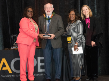 An older gentleman receives an award among a group at a conference.