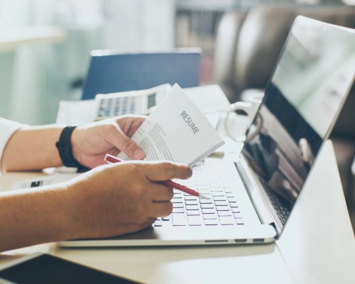 A picture of hands holding a resume in front of a laptop.