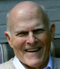 An image of an older man wearing a sweater and oxford shirt smiling at the camera.