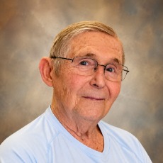 Headshot of an older gentleman wearing glasses in a blue shirt looking at the camera.